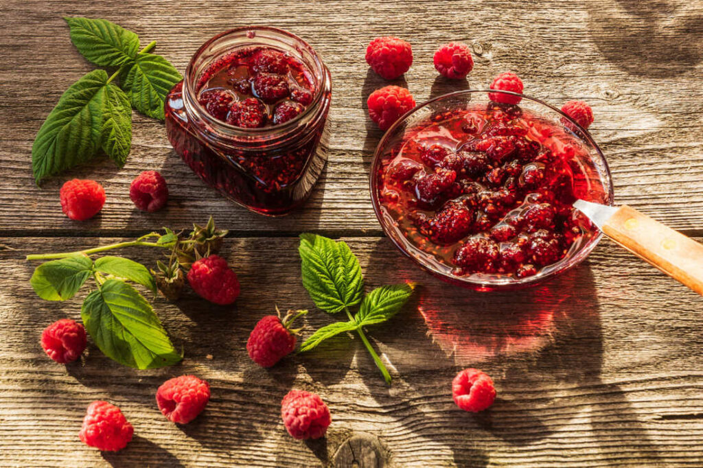 bol si borcan cu dulceata de zmeura pe masa rustica cu zmeura proaspata