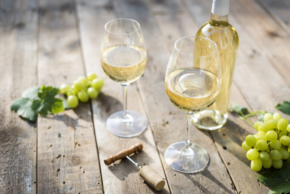 pahare cu vin alb pe masa langa o sticla de vin alb si struguri