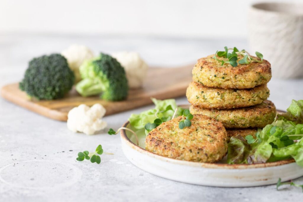 Burgeri vegetarieni pe farfurie ceramica alaturi de salata, broccoli si conopida