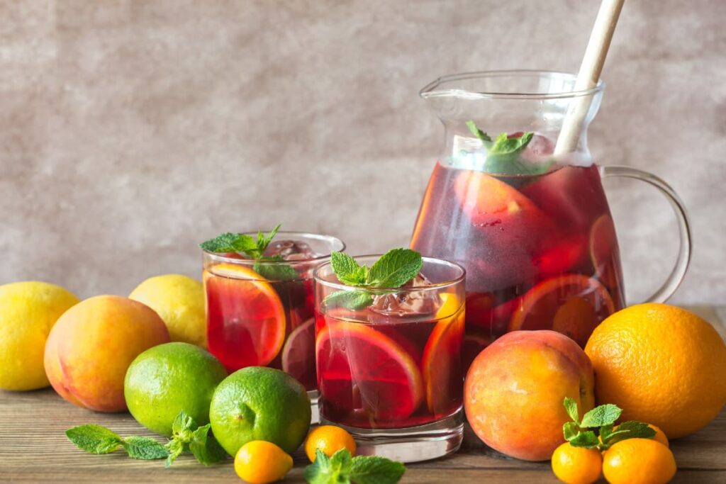 Carafa si pahare cu sangria alaturi de fructe pe blat din lemn
