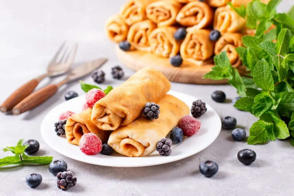 Clatite traditionale rulate pe farfurie alaturi de fructe de padure