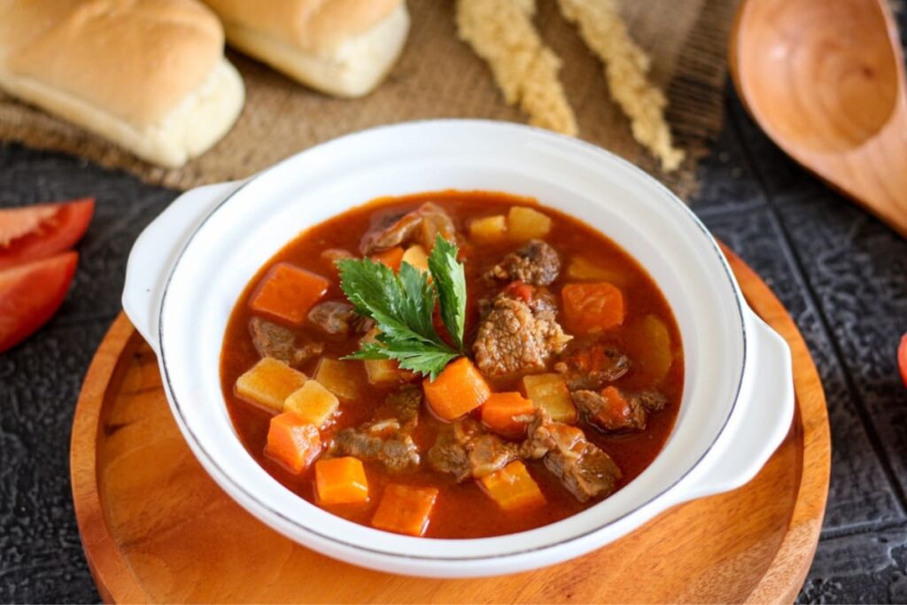 Gulas de vita unguresc in bol alb pe tava din lemn