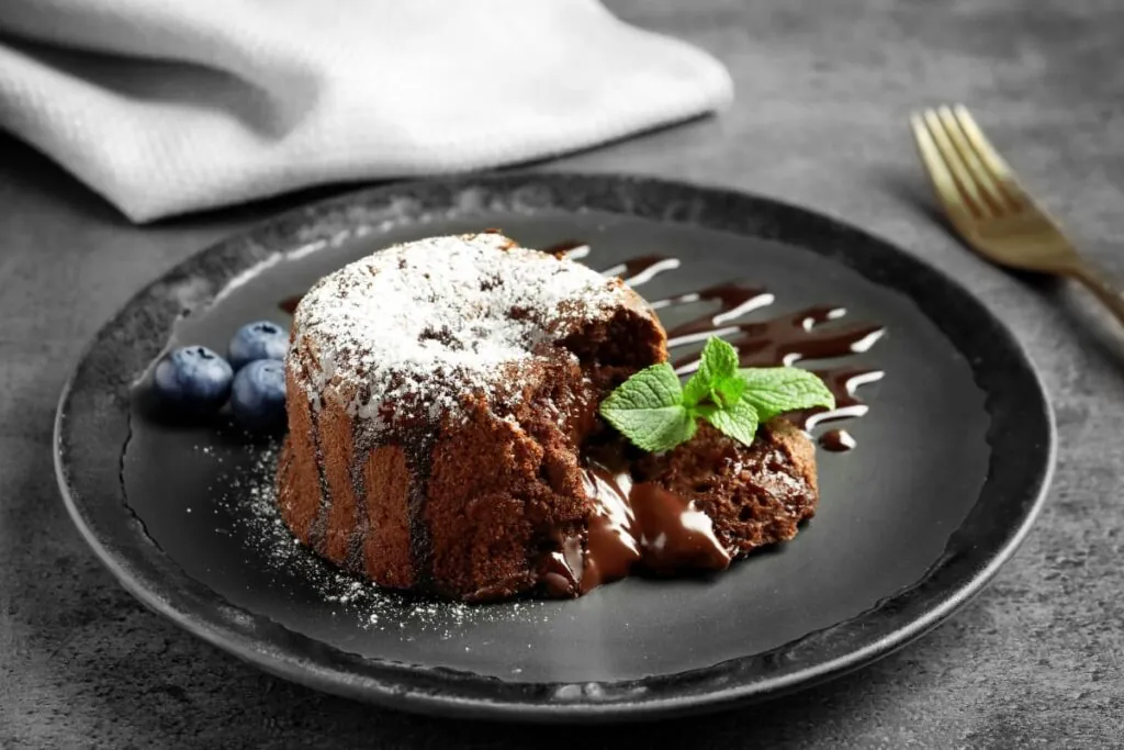 Lava cake pe farfurie neagra cu zahar pudra, menta si afine
