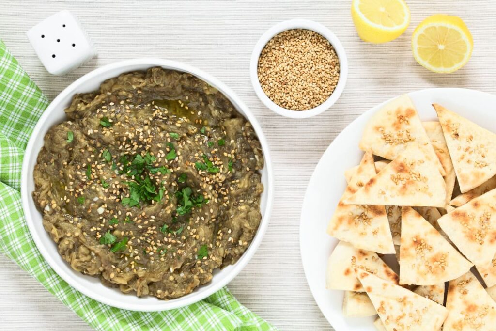Salata de vinete clasica in bol alaturi de bucati de lipie si seminte de susanf