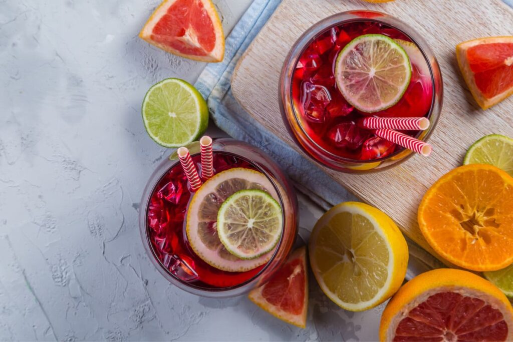 Sangria in pahare decorate cu paie alaturi de fructe citrice