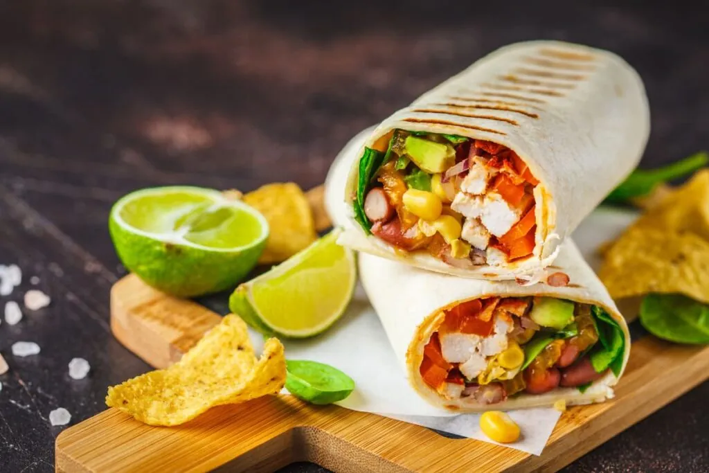 burrito cu pui si legume pe tocator din lemn alaturi de lime
