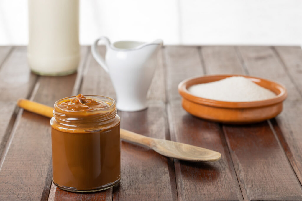 borcan cu dulceata de lapte alaturi de zahar si lapte pe masa rustica