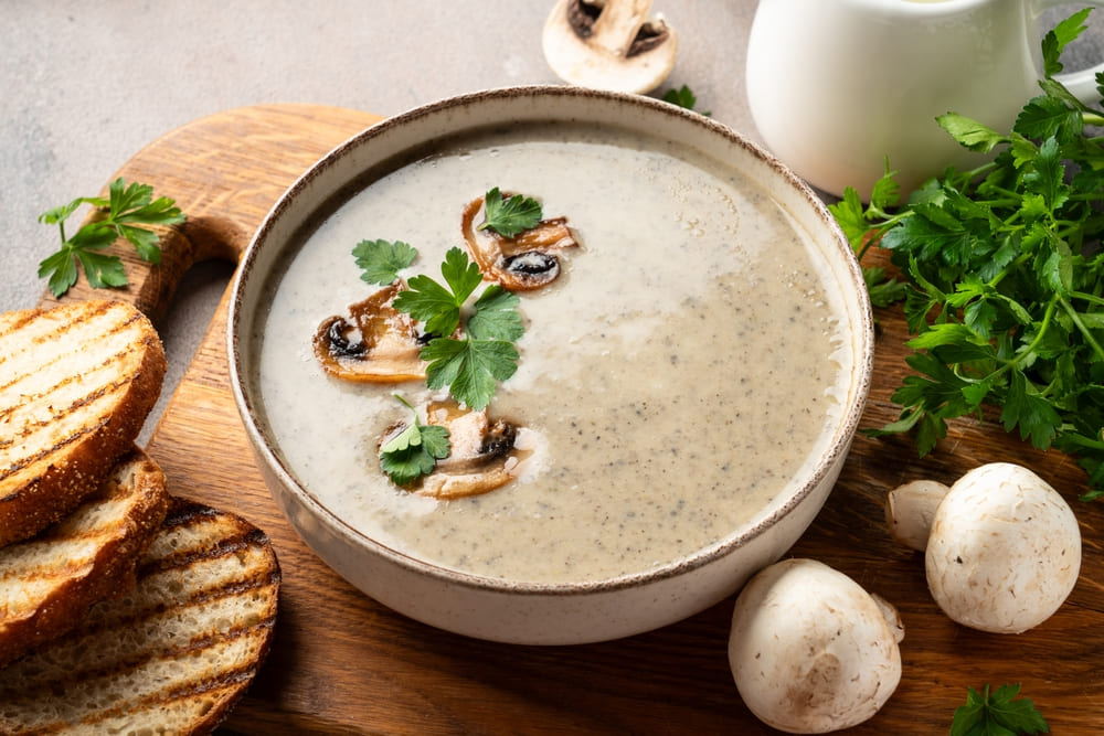 supa crema de ciuperci servita intr-un bol alaturi de paine prajita si patrunjel
